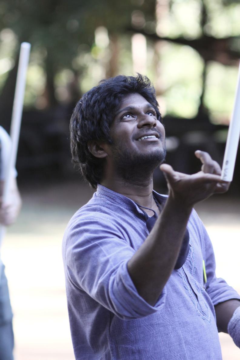 Young man of Indian descent looks up at sky while balancing stick on his finger.